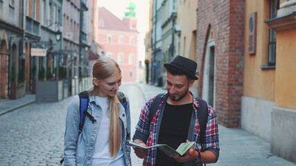 Two young tourists checking map while walking on main tourist street. They going sightseeing early in the morning.