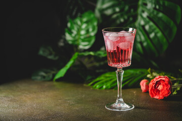 Red drink cocktail or lemonade with ice in a glass on dark background.