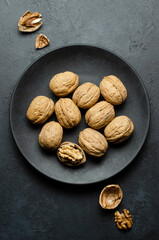 Walnuts in a plate on a dark concrete background. Nuts are a source of vegetable protein and vitamins. Flat top view, copy space.