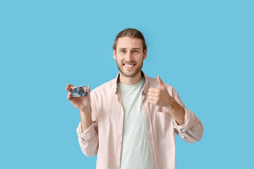 Handsome young man with gift card showing thumb-up gesture on color background