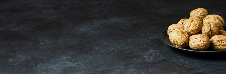 Walnuts in a plate on a dark concrete background. Nuts are a source of vegetable protein and vitamins