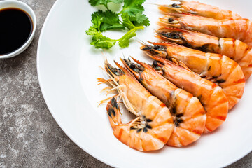 A plate of boiled black tiger prawns and seasoning sauce on cement shading