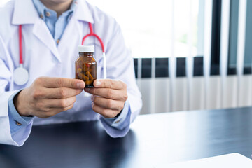 A doctor or pharmacist sits at a desk, holds or shows a bottle of medicine in his hand and writes a prescription explaining its properties. Concept of medical treatment, pharmacy or health insurance