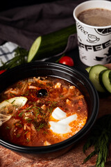 hodgepodge soup on a wooden board with cucumbers, tomatoes, herbs, coffee and napkins on a black background