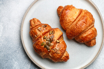 Freshly baked homemade croissants for breakfast close-up. Traditional and whole-grain croissant with pumpkin seeds in a gray plate on a concrete or stone background. Selective Focus