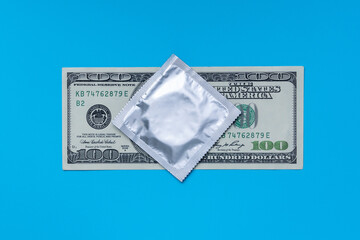A condom lies on a 100 dollar bill lying on a blue background