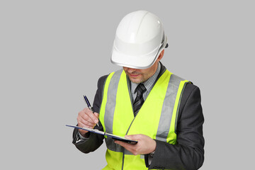 Man in suit and reflective vest with white hardhat on his head performs inspection and notes on paper. Isolated on gray background