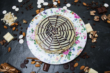 Cake with white and dark chocolate, cream, frosting, nuts, cinnamon and almonds view from the top, copy space, on a multi-colored plate, on a dark concrete background