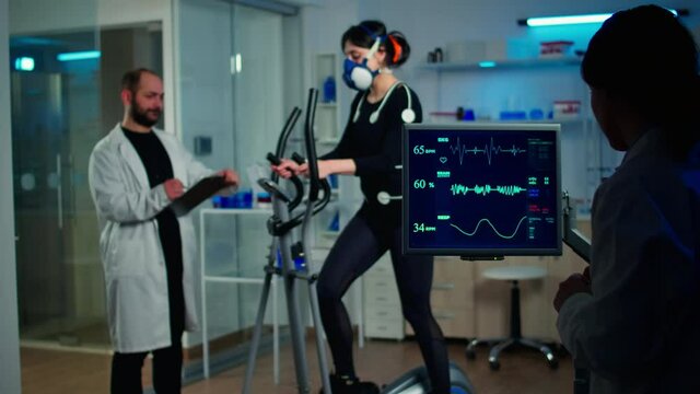 Professional scientist analysing EKG results looking at monitor examining heart rate of athlete. Team of researchers monitoring endurance, vo2 max, psychological resistance in science sport laboratory