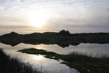 the sand dunes of ynyslas wales reflected in the flooded waters  next to the road 
