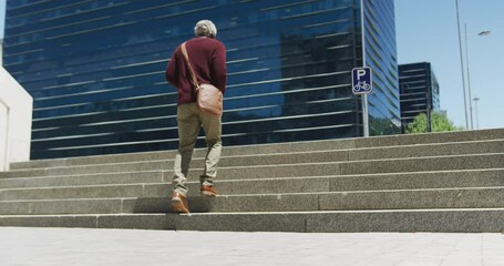 Rear view of african american senior man walking up the stairs at corporate park - Powered by Adobe