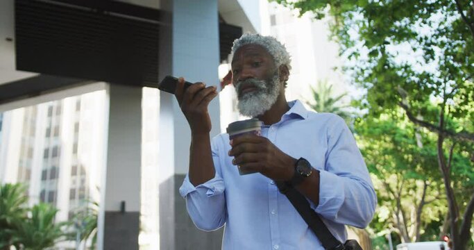 African american senior man drinking coffee and talking on smartphone in corporate park