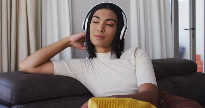 Gender fluid male wearing headphones listening to music while sitting on the couch at home