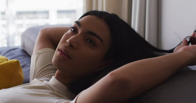 Close up of gender fluid male playing with hair while lying on the couch at home
