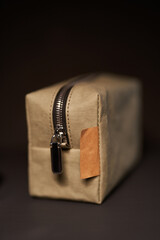 Zero waste concept. Green reusable paper travel cosmetic pouch with metal zipper and brown label on black background