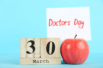 Text Doctor's Day with red apple and cube calendar on blue background
