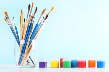 Obraz premium Artistic brushes in glass and colorful gouache paints on blue background