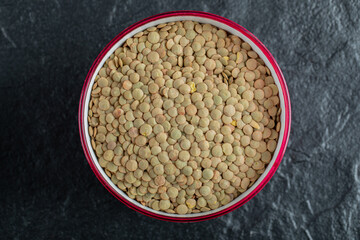 A red bowl with dried raw lentils on a dark background