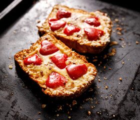 Warm cheese toast with red pepper on a black background, close-up. An idea for a Valentine's Day food