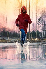 Boy teenager in a jacket and boots jumps, runs through the puddles in the cold autumn