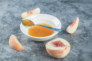 A white plate with jam and peaches on a gray tablecloth