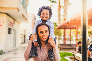 Young black mother and son together have fun and enjoy the playhood at the park  mommy take litthe boy on her shoulder - happiness and love family concept
