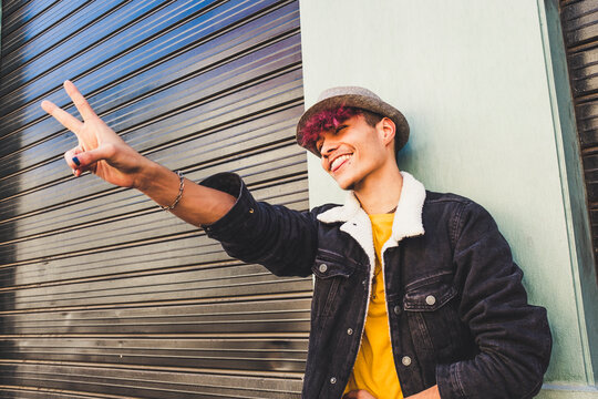 Happy young teenager boy do victory sign with hand and fingers - portrait of joyful and cheerful man have fun and enjoy modern limmennial lifestyle - alternative diversity people in the city