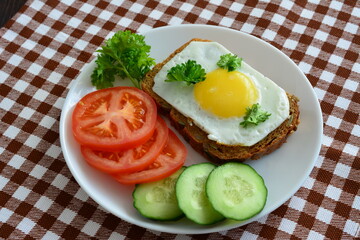 sandwich with fried egg on the white plate with tomato and cucumber slices and whole grain bread
