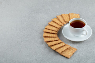 A cup of aroma tea with crackers on a gray background