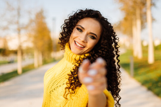 In a yellow bright sweater, a girl with dark curls happily pulls her hands forward. High quality photo