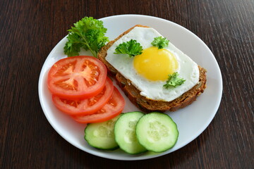 sandwich with fried egg on the white plate with tomatoes and cucumber and whole grain bread on the wooden background