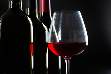 elegant Wine bottles and a glass with red wine on a dark glossy background.