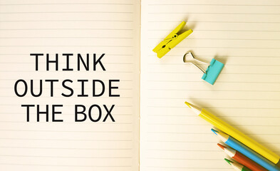 THINK OUTSIDE THE BOX on notebook surrounded with colorful office supplies.