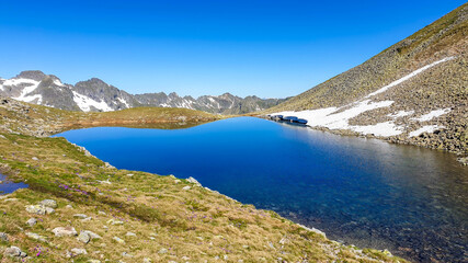 Obraz premium Clear, navy blue lake hiding between tall mountain peaks. Some of the slopes are still covered with snow. In the back here is another mountain range. Clear and bright day. Perfect condition for hiking
