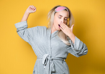 Girl yawning. Sleepy young woman yawns, model wearing nightie - night dress, isolated on yellow background. Studio shot