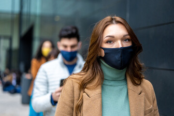 beautiful eyes of a young redhead woman looking at the camera, tired and sad expression under facemask in quarantine time, crowd in queue waiting in line