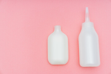 a white tube with paint and a bottle with a convenient applicator for the developing emulsion for self-dyeing hair at home on a pink background. saving time and money. home beauty salon.
