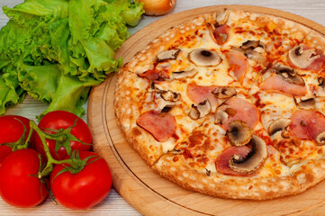 Pizza with ham, mushrooms and cheese on a board with tomatoes and green salad