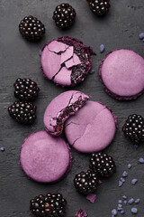 Set of violet macarons and blackberries on dark concrete background. Overhead view, close up