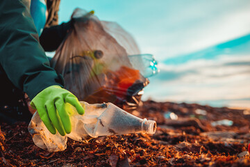 A worker in rubber gloes collects a plastic bottle on a beach. Hand close-up. The concept of Earth...
