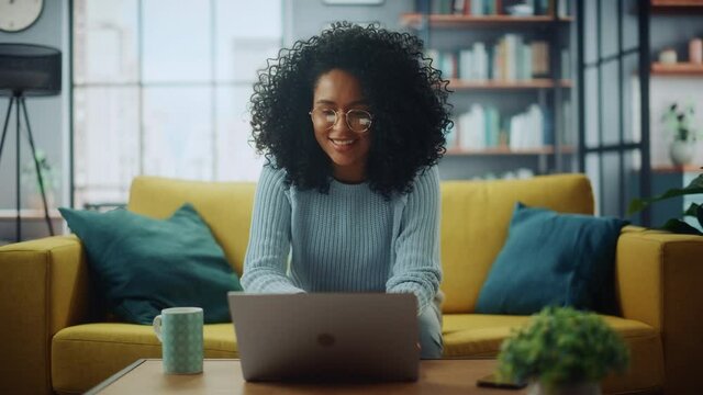 Portrait of a Beautiful Authentic Latina Female in a Stylish Cozy Living Room Using Laptop Computer at Home. She's Browsing the Internet and Checking Videos on Social Networks and Having Fun.