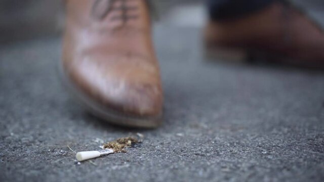 Close-up of male foot in brown stylish shoe stomping on burning cigarette fallen on asphalt. Unrecognizable man quenching cigarette and leaving. Unhealthy lifestyle and environmental pollution.