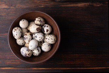 Fresh quail eggs in a bowl on a dark wooden background, rustic style.