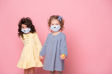 two girls in protective mask with colored eggs holding hands on pink background. Covid easter concept