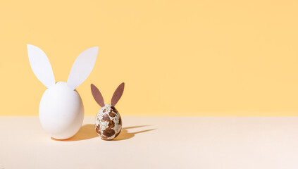 Fototapeta na wymiar One chicken egg and quail with easter bunny ears on beige and yellow background, modern isometric easter concept.