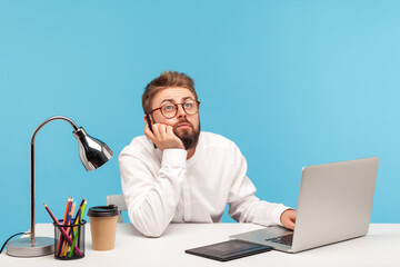 Bored bearded man graphic illustrator sitting at workplace with laptop and tablet holding stylus in...