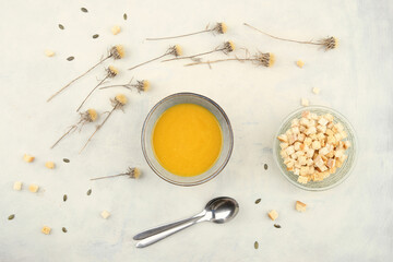 Pumpkin cream soup and  bread croutons, top view. Autumn or winter pumpkin soup on table with dried flowers.