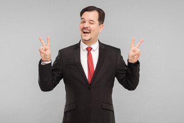 Businessman showing finger nomber four toothy smiling and wink. indoor studio shot. isolated on gray background. handsome businessman with black suit, red tie and mustache looking at camera.