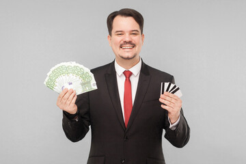 Businessman holds a lot of euros and a lot of bank cards. Indoor, studio shot, isolated on gray background