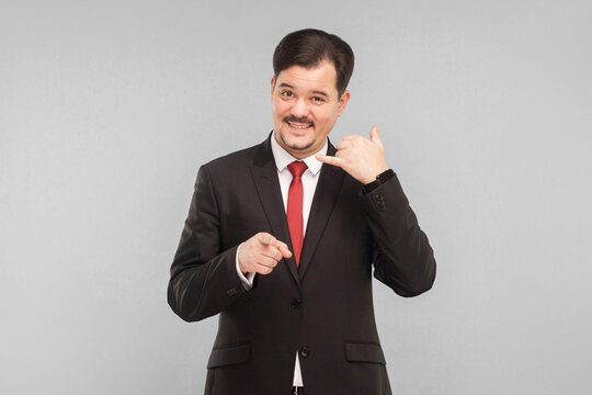 Call center. Businessman showing phone sign and smiling. indoor studio shot. isolated on gray background. handsome businessman with black suit, red tie and mustache looking at camera.